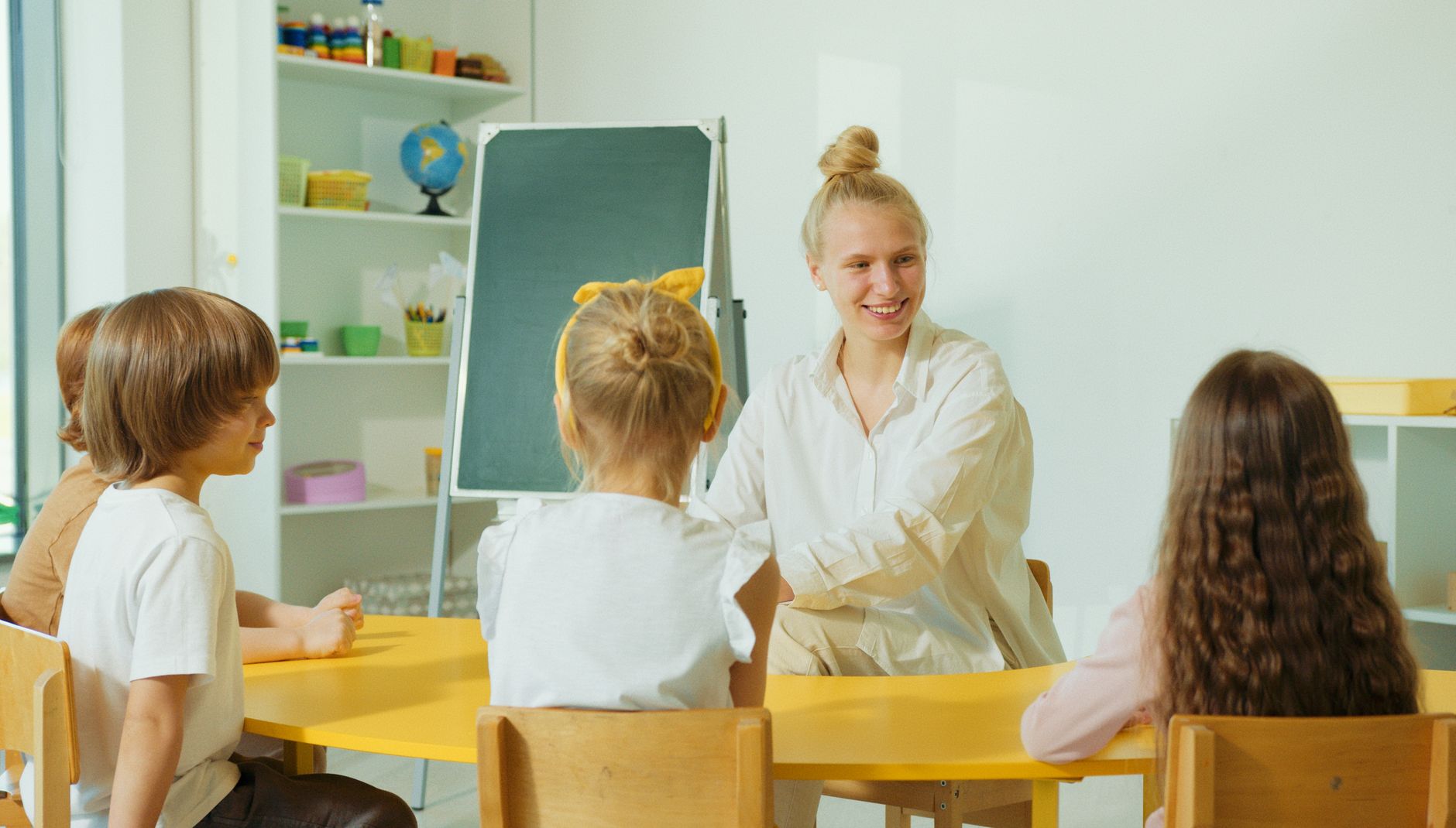A teacher sitting with a small group of preschool children during circle time in a colorful classroom