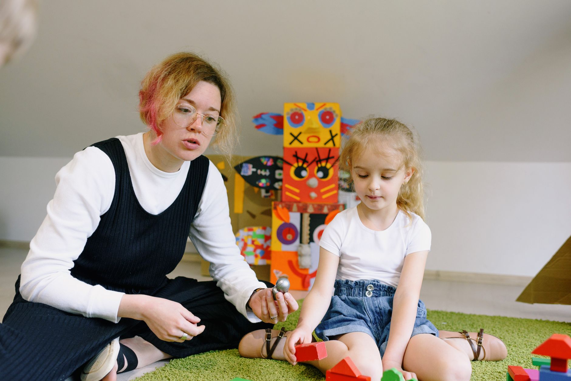 A teacher and a young child playing together with colorful wooden blocks indoors