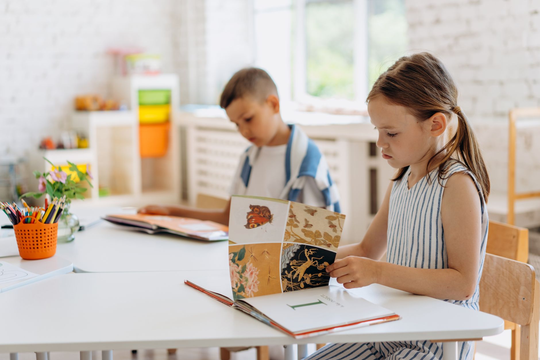 Two children reading books together at a classroom table